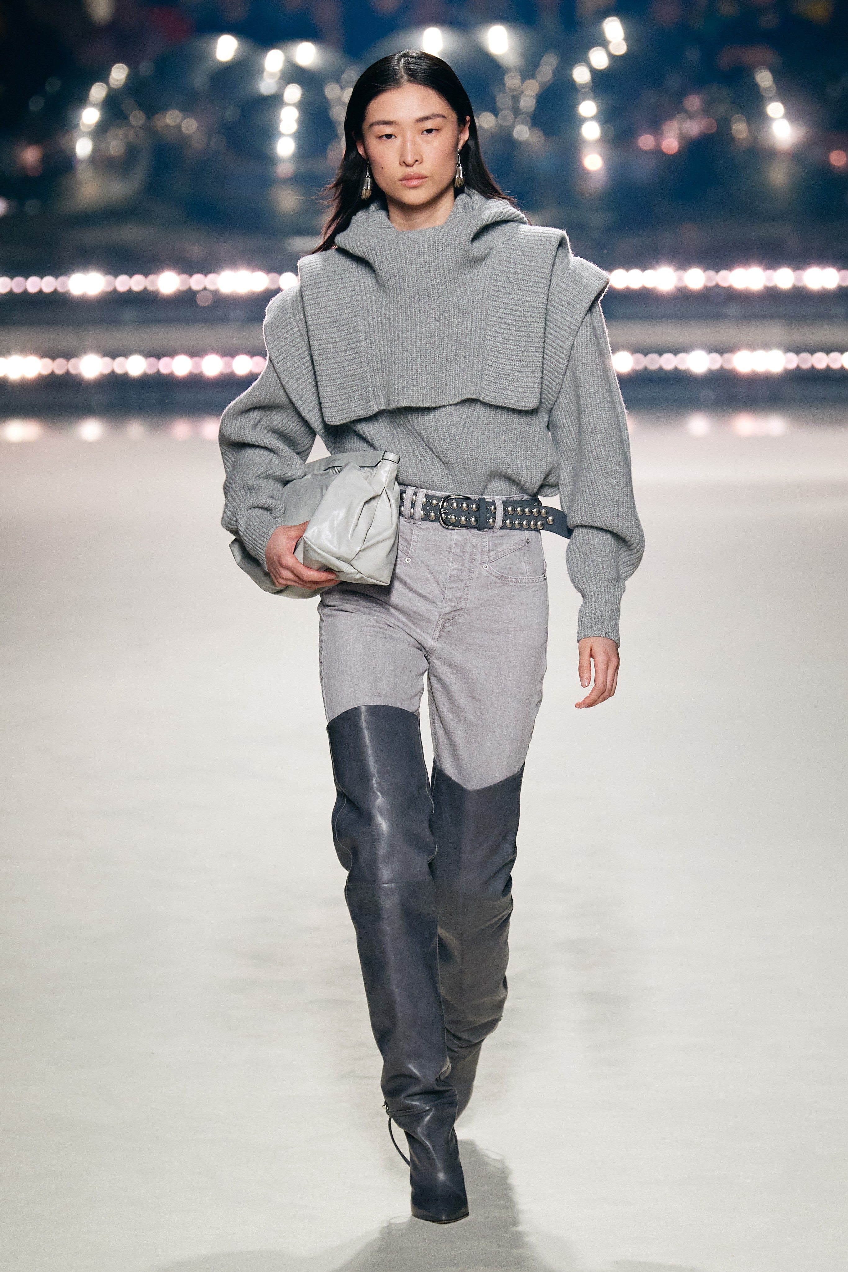 Confort et style émanent de cette collection hivernale Isabel Marant. Un pull en maille grise à la coupe audacieuse s’associe à un jean mastic et des cuissardes larges gris foncé.