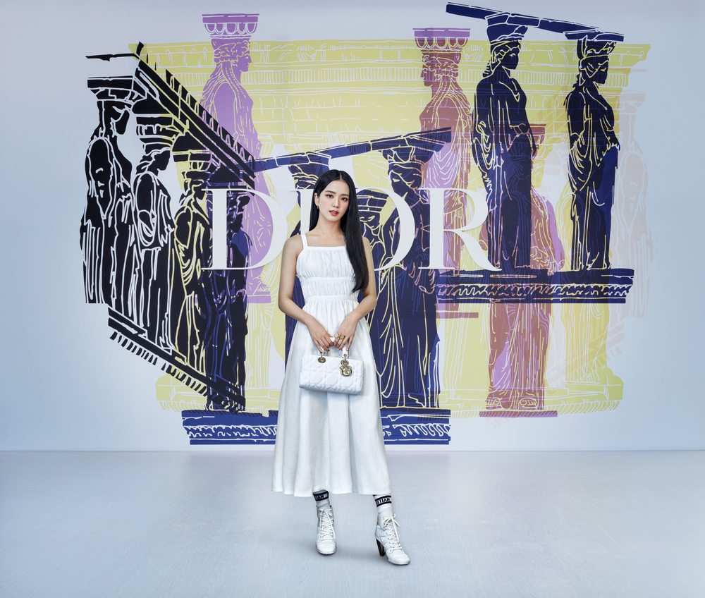 Jisoo wore a Dior Cruise 2022 white linen dress with Dior socks and Dior Zenith sneakers.  She also wore a white micro mesh fabric Lady Dior East West bag. 