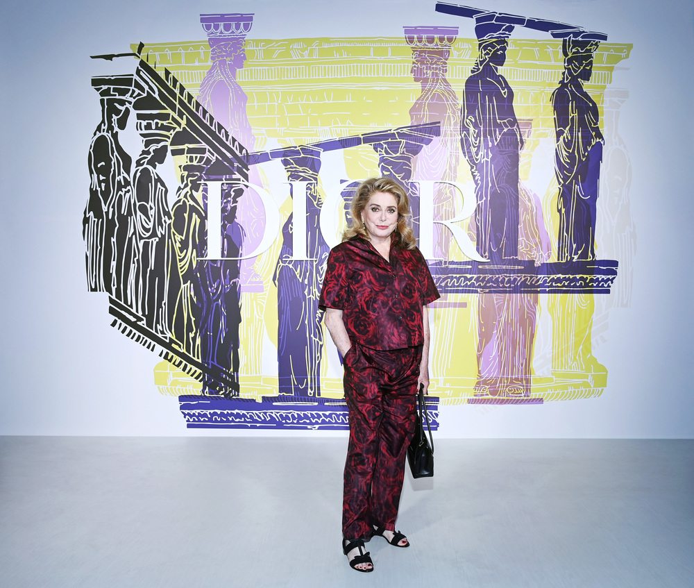 Catherine Deneuve wore a Dior Winter 2021-2022 printed red and black silk blouse and pants. She also wore Dior sandals.
