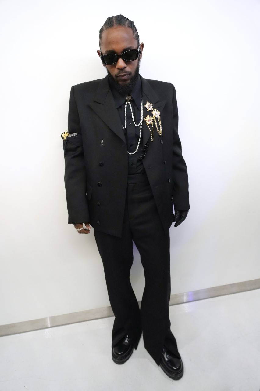 Kendrick Lamar is wearing a double-breasted suit with jewelry buttons and a silk shirt, with a pair of gloves and boots designed by Virgil Abloh for Louis Vuitton.