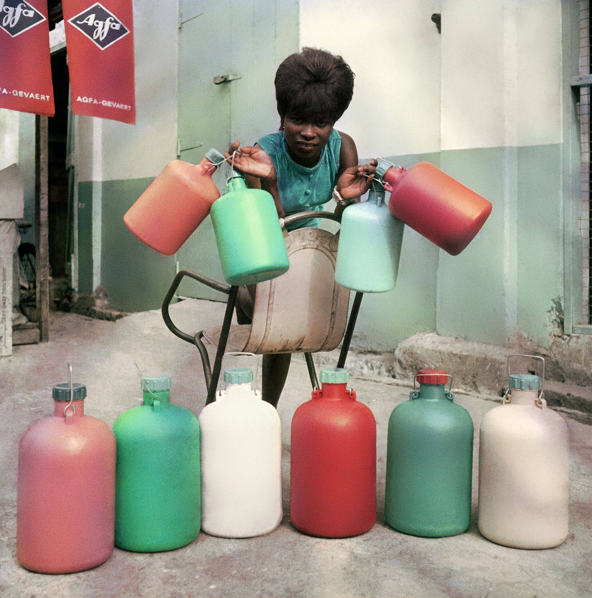 James Barnor, “Une employée du magasin Sick Hagemeyer avec des bouteilles chimiques de chambre noire utilisées comme guide pour le laboratoire de traitement des couleurs”, Accra (c. 1970) © James Barnor
