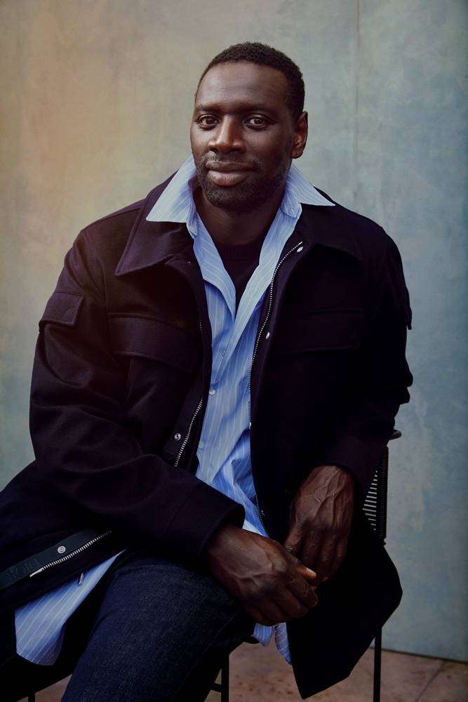 Omar Sy, Portait taken on July 25 2022 at Studio Zéro, rue Robert-Blache, Paris Xe. Parka in cachemere, shirt in coton poplin, t-shirt in coton and denim pants, Collection Homme, DIOR. Hair and make-up : Barbara Guillaume at Forward Artists. Director's assistant : Oliver Vaughn. Barber : Don Campbell. Retouche : Amanda Sperry