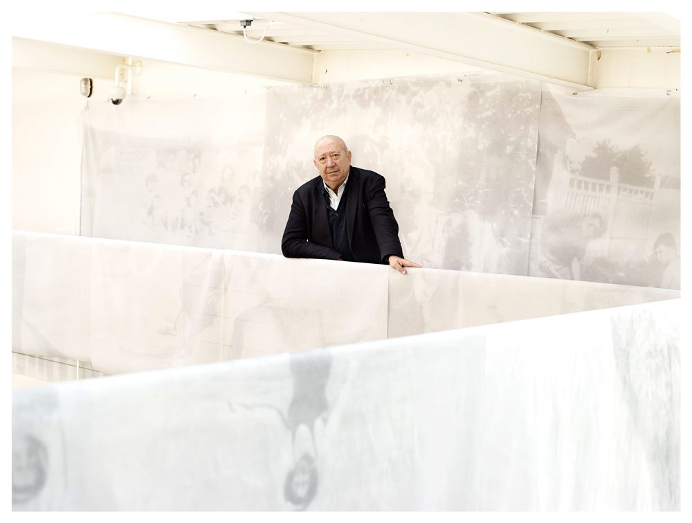 Christian Boltanski sur la mezzanine de son atelier, entouré de tissus presque transparents sur lesquels l’artiste a imprimé les photographies d’un album de famille imaginaire, L’Album de la famille D. L’ensemble de ces voiles forme un labyrinthe au sein duquel le spectateur est actuellement invité à circuler, au cœur de l’espace parisien de la Galerie Marian Goodman.