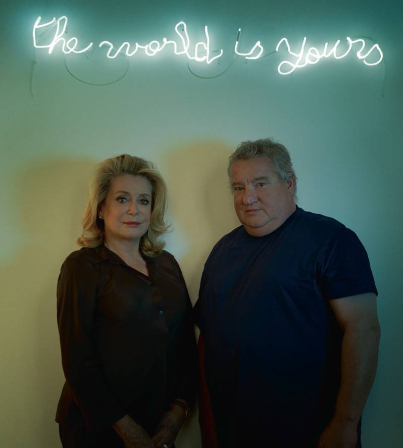 Catherine Deneuve et Claude Lévêque à la galerie Kamel Mennour à Paris, sous un néon de l’artiste, The World is Yours, (2013), néon blanc, 19 x 116 cm (©ADAGP Claude Lévêque).