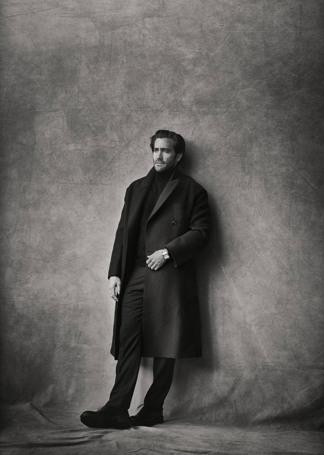 Jake Gyllenhaal porte un manteau croisé en laine et cachemire, un pull en mérinos, un pantalon en laine et des derbys Giorgio Armani, et une montre “Santos de Cartier”, Cartier.