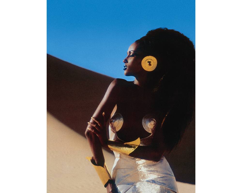 ERG MEHEDJEBAT (SAHARA ALGÉRIEN), 1985. Iman Abdumajid en "Seins d'or massif” de Mugler